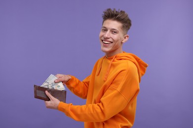 Happy man putting money into wallet on purple background