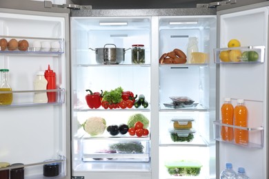 Photo of Modern open refrigerator full of different products indoors