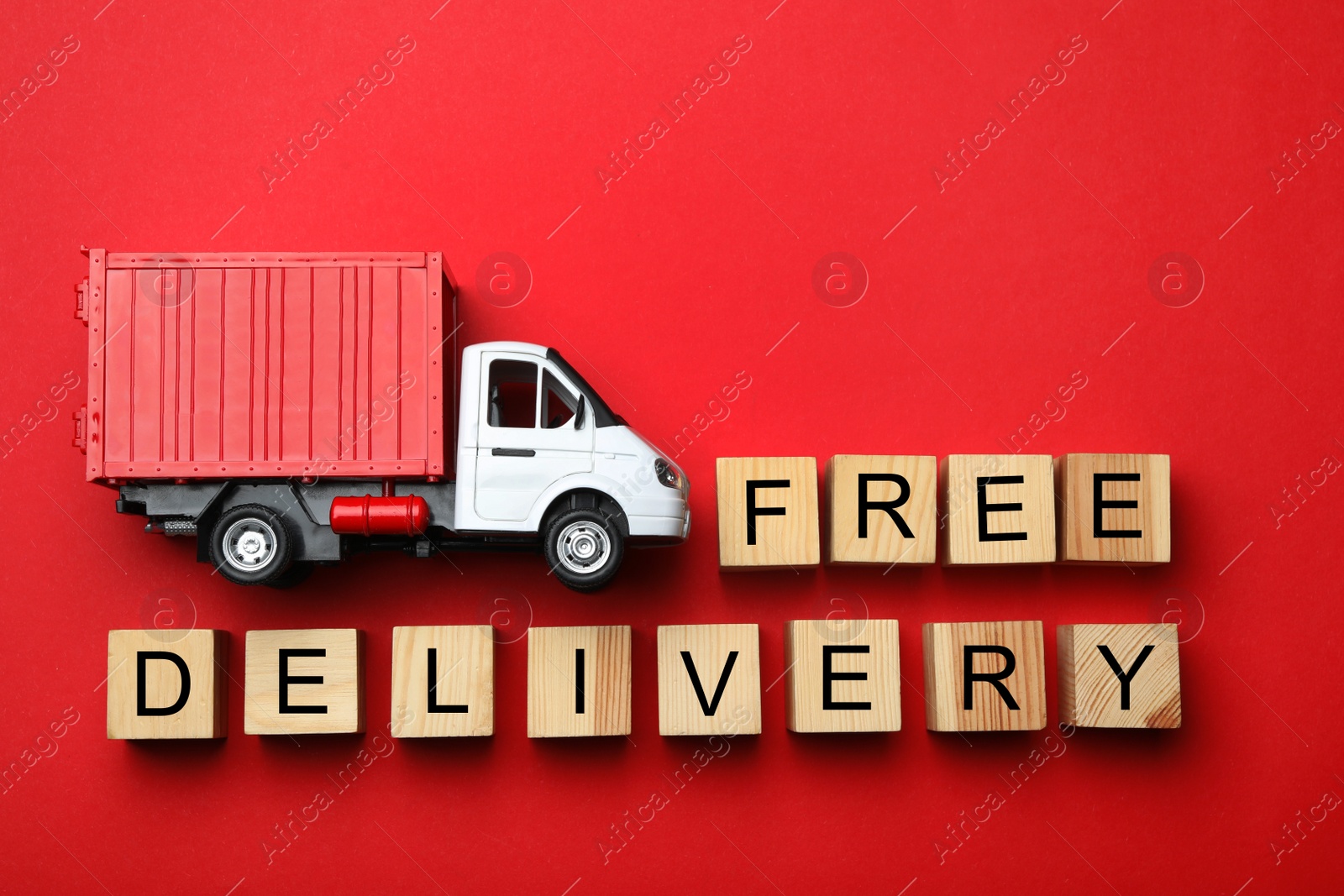 Photo of Flat lay composition of toy truck with words FREE DELIVERY on red background. Logistics and wholesale concept