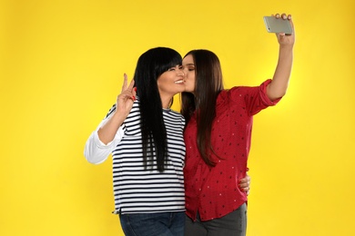 Young woman and her mother taking selfie on color background