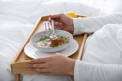 Photo of Sick young man eating soup to cure flu in bed at home, closeup