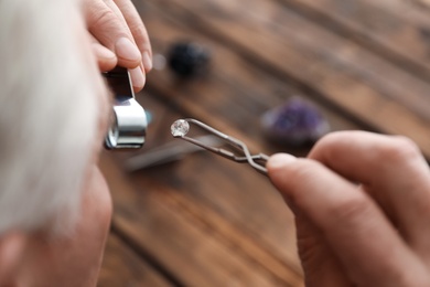 Photo of Male jeweler evaluating precious gemstone in workshop, closeup