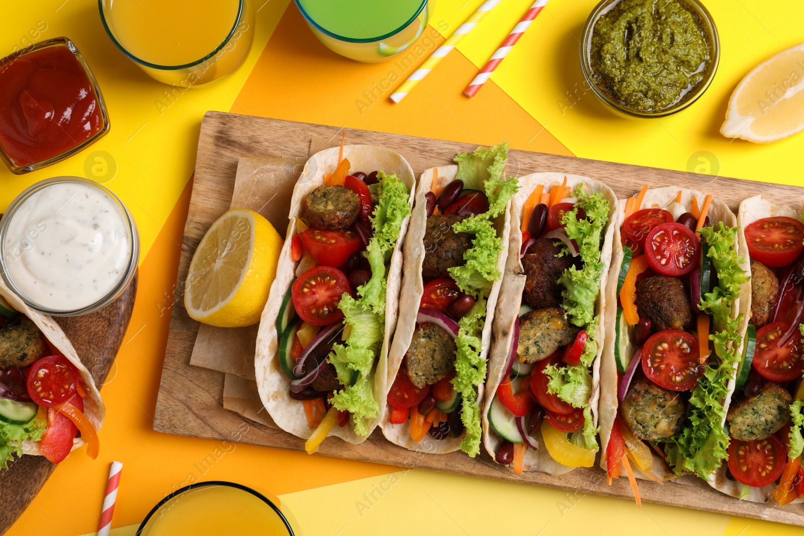 Photo of Many delicious vegetarian tacos served on yellow table , flat lay