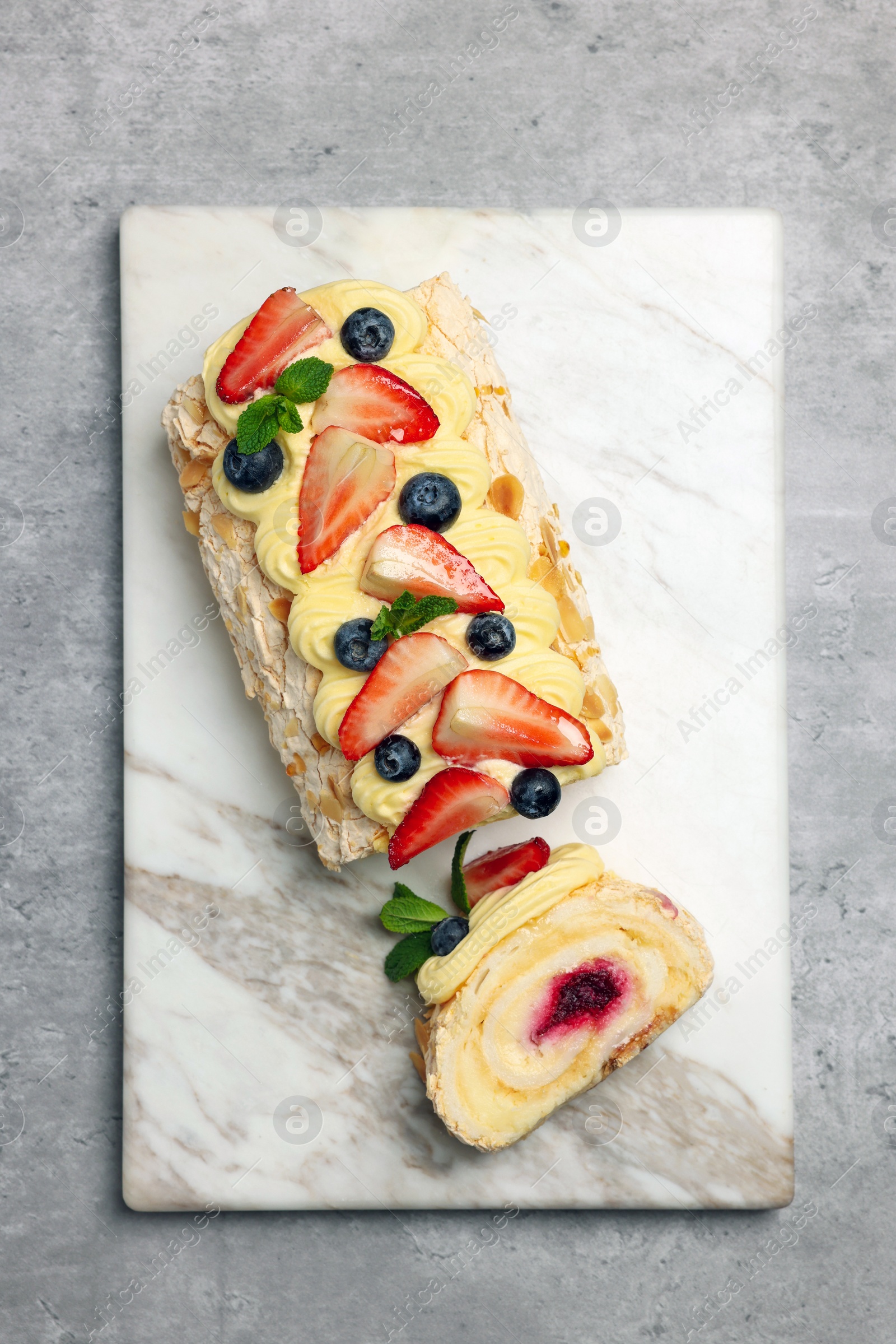 Photo of Tasty meringue roll with jam, cream, strawberry, blueberry and mint on light grey table, top view