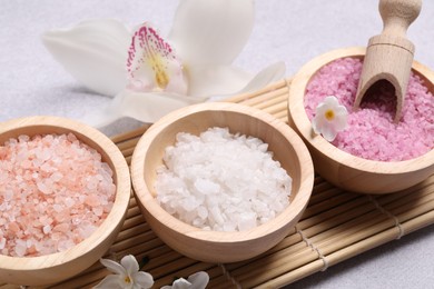 Photo of Different types of sea salt and flowers on light table, closeup. Spa products