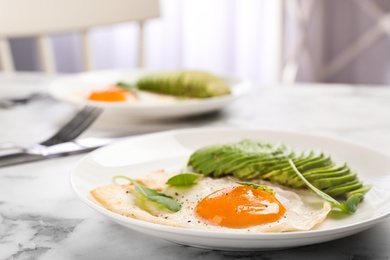 Tasty breakfast with fried egg and avocado on white marble table