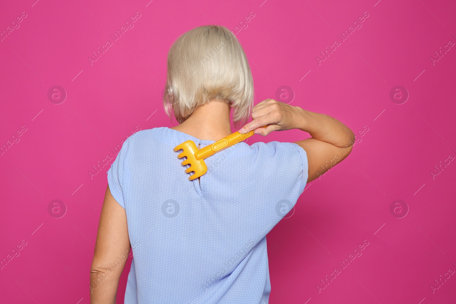 Photo of Mature woman scratching back with toy rake on color background. Annoying itch