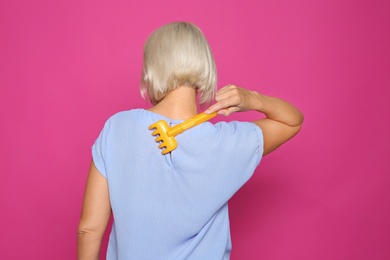 Photo of Mature woman scratching back with toy rake on color background. Annoying itch