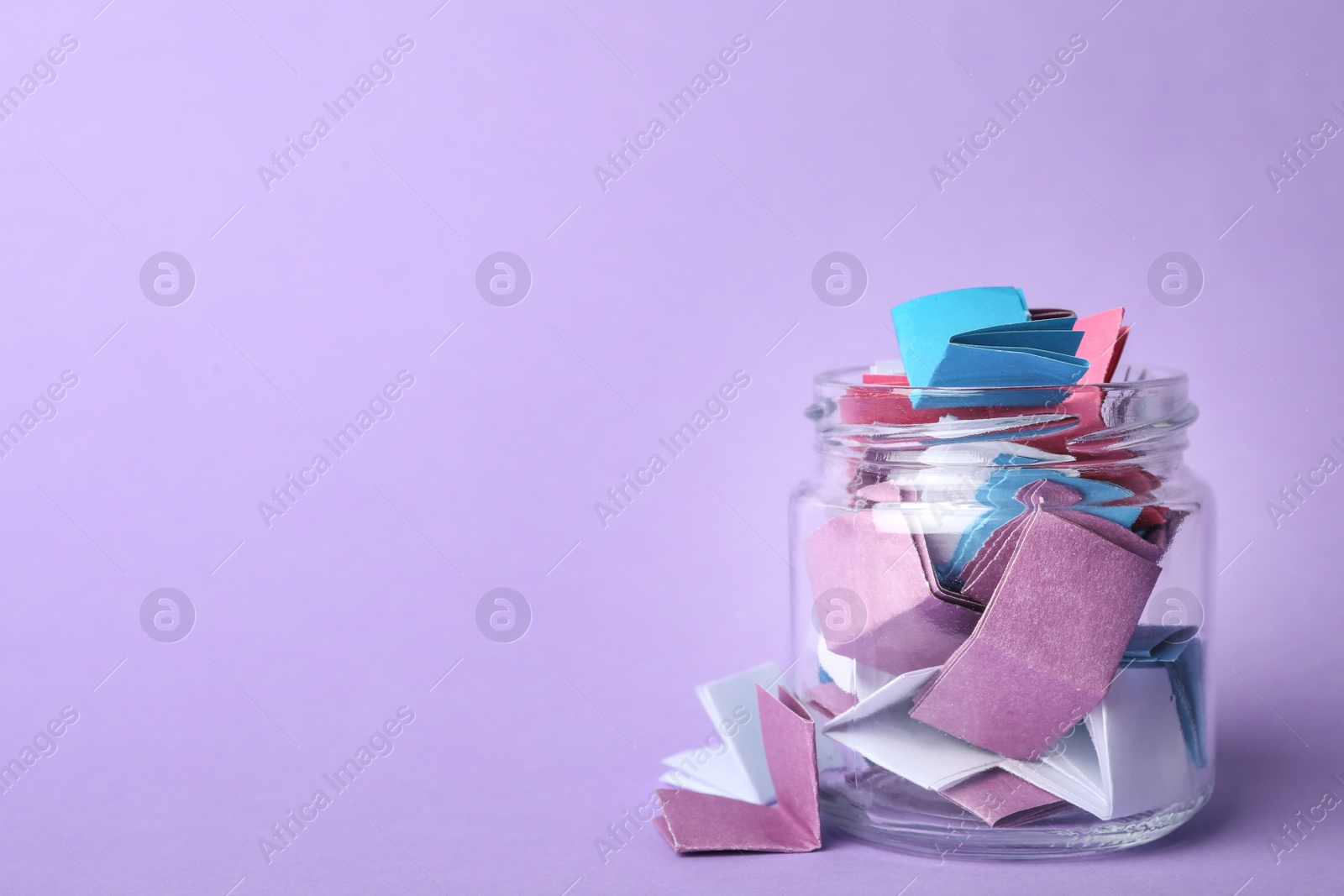 Photo of Glass jar full of folded paper sheets on violet background, space for text