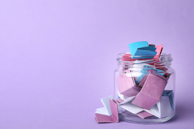 Photo of Glass jar full of folded paper sheets on violet background, space for text