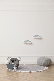 Photo of Wicker basket, toys and pouf near white wall indoors. Interior design
