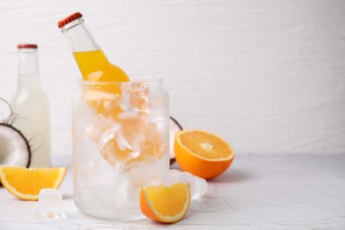 Photo of Tasty kombucha in bottles, glass with ice and fresh fruits on white table, space for text