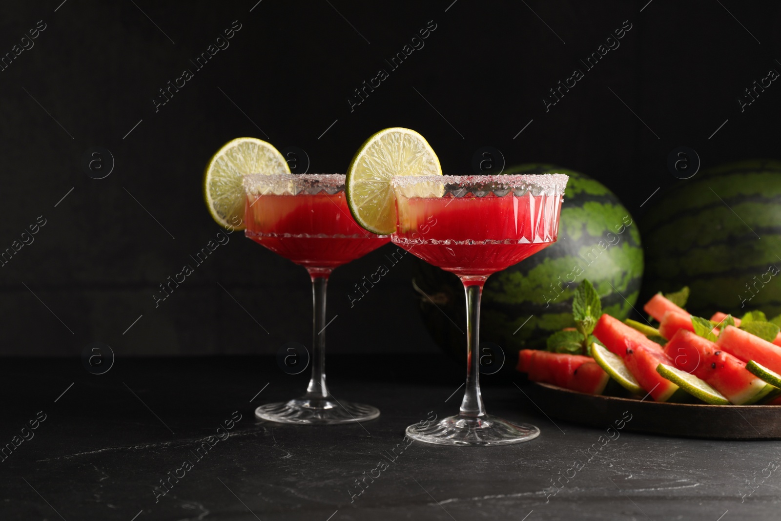 Photo of Cocktail glasses of delicious fresh watermelon juice with lime and sugar rim on black table