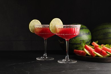 Cocktail glasses of delicious fresh watermelon juice with lime and sugar rim on black table