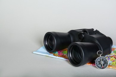 Photo of Modern binoculars, compass and map on grey background, space for text