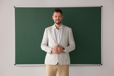 Happy teacher standing at blackboard in classroom