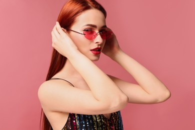 Beautiful woman with red dyed hair and sunglasses on pink background