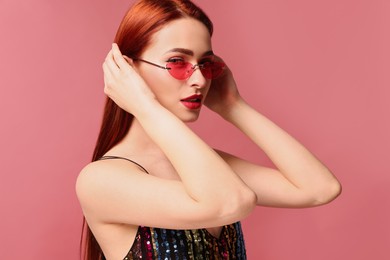 Photo of Beautiful woman with red dyed hair and sunglasses on pink background