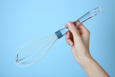 Woman holding whisk on light blue background, closeup