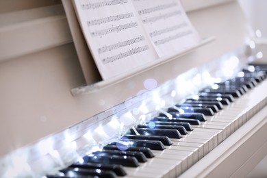 Photo of Glowing fairy lights on piano keys, closeup. Christmas music