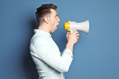 Young man shouting into megaphone on color background