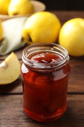 Photo of Tasty homemade quince jam in jar and fruits on wooden table, closeup