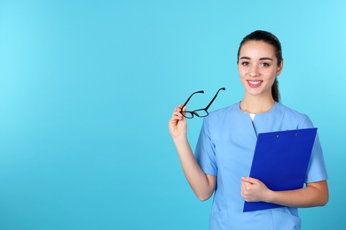 Young medical student with clipboard and glasses on color background. Space for text