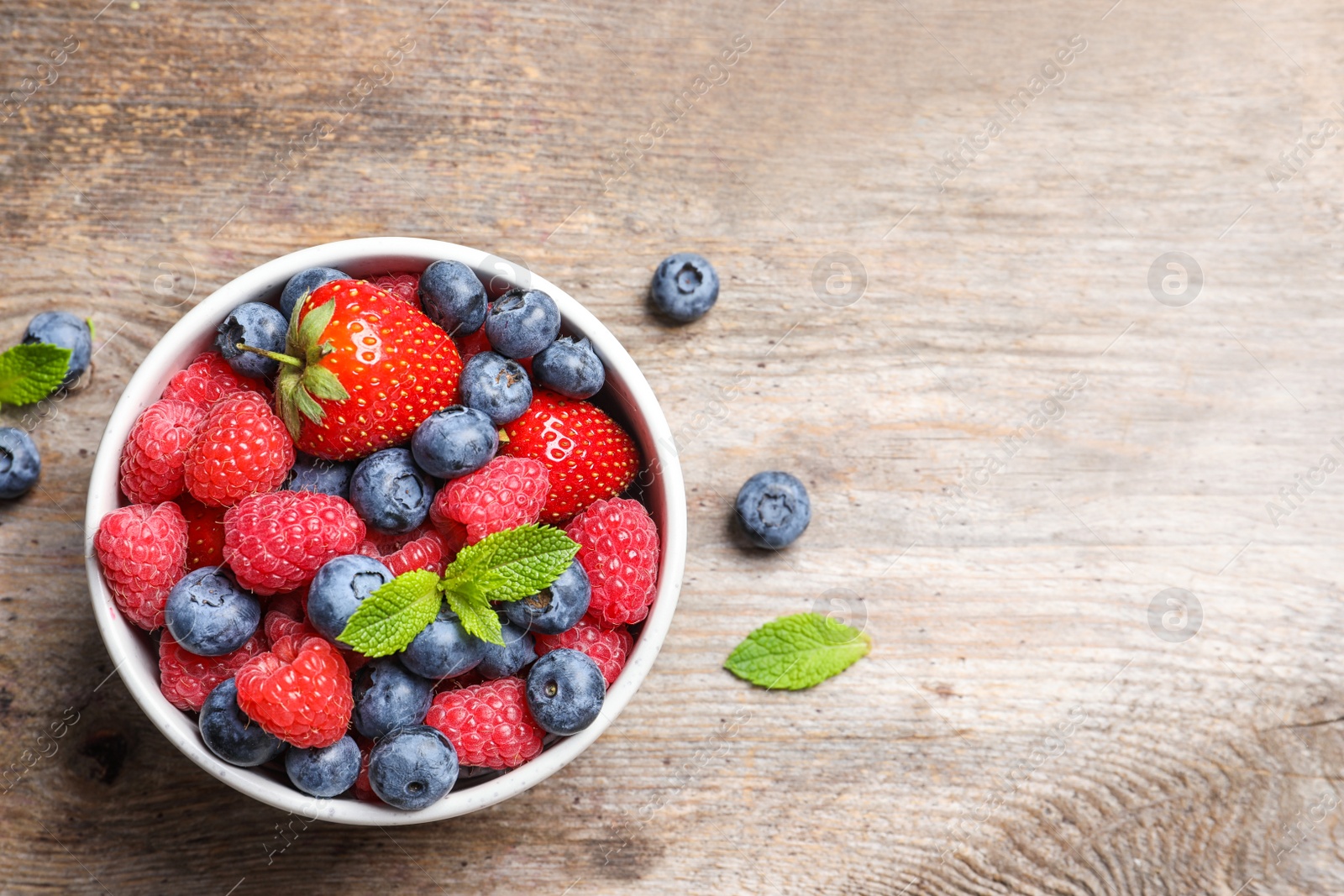 Photo of Bowl with raspberries, strawberries and blueberries on wooden table, top view