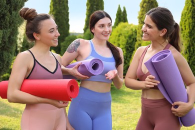 Photo of Young women in sportswear with yoga mats talking outdoors
