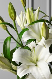 Photo of Beautiful lily flowers near light grey wall, closeup