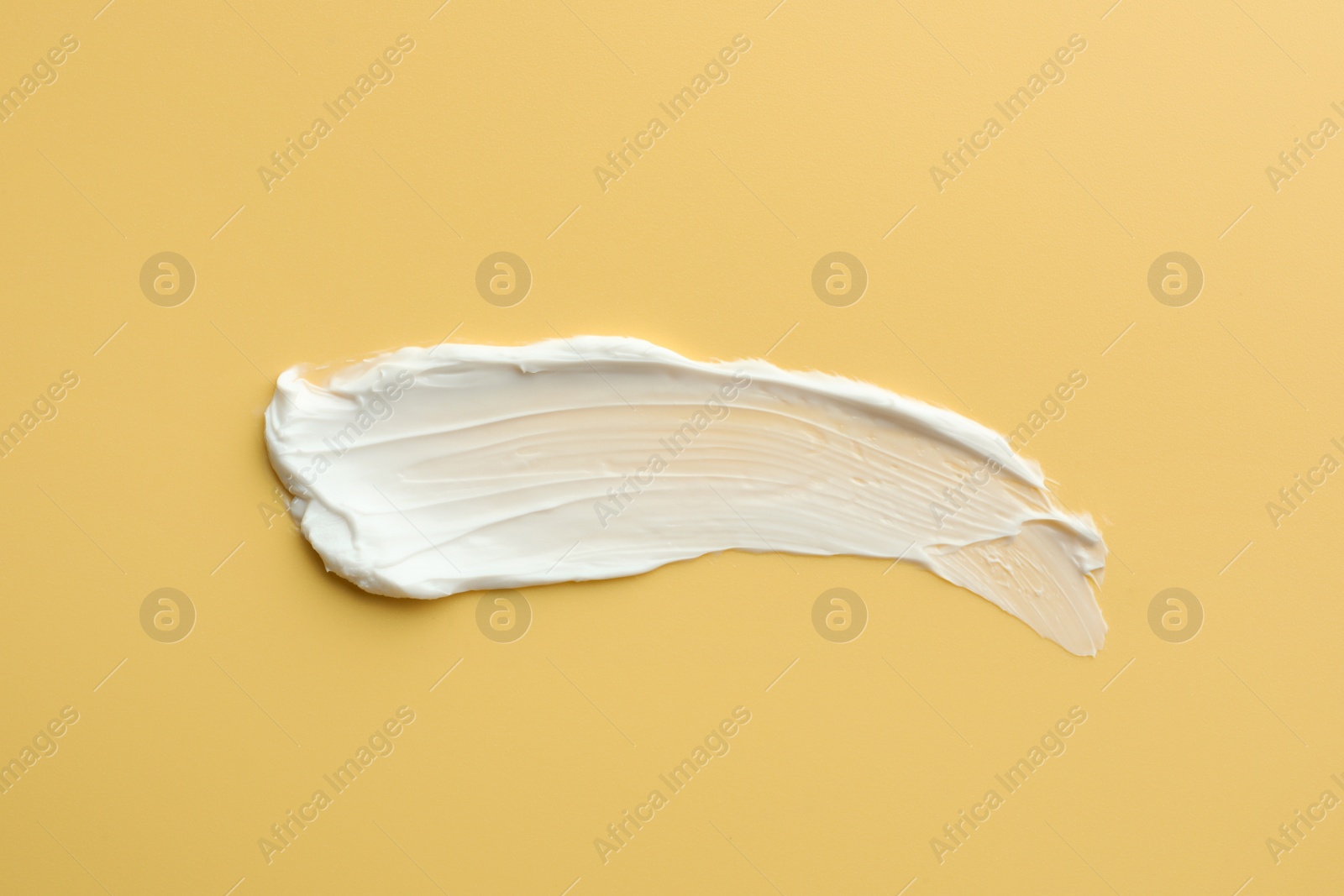 Photo of Sample of face cream on yellow background, top view