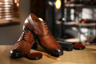 Pair of shoes and items for footwear care on wooden table in workshop