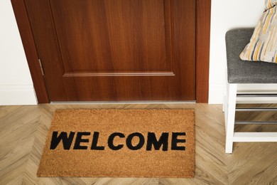 Photo of New clean brown mat with word Welcome near entrance door and shoes shelf