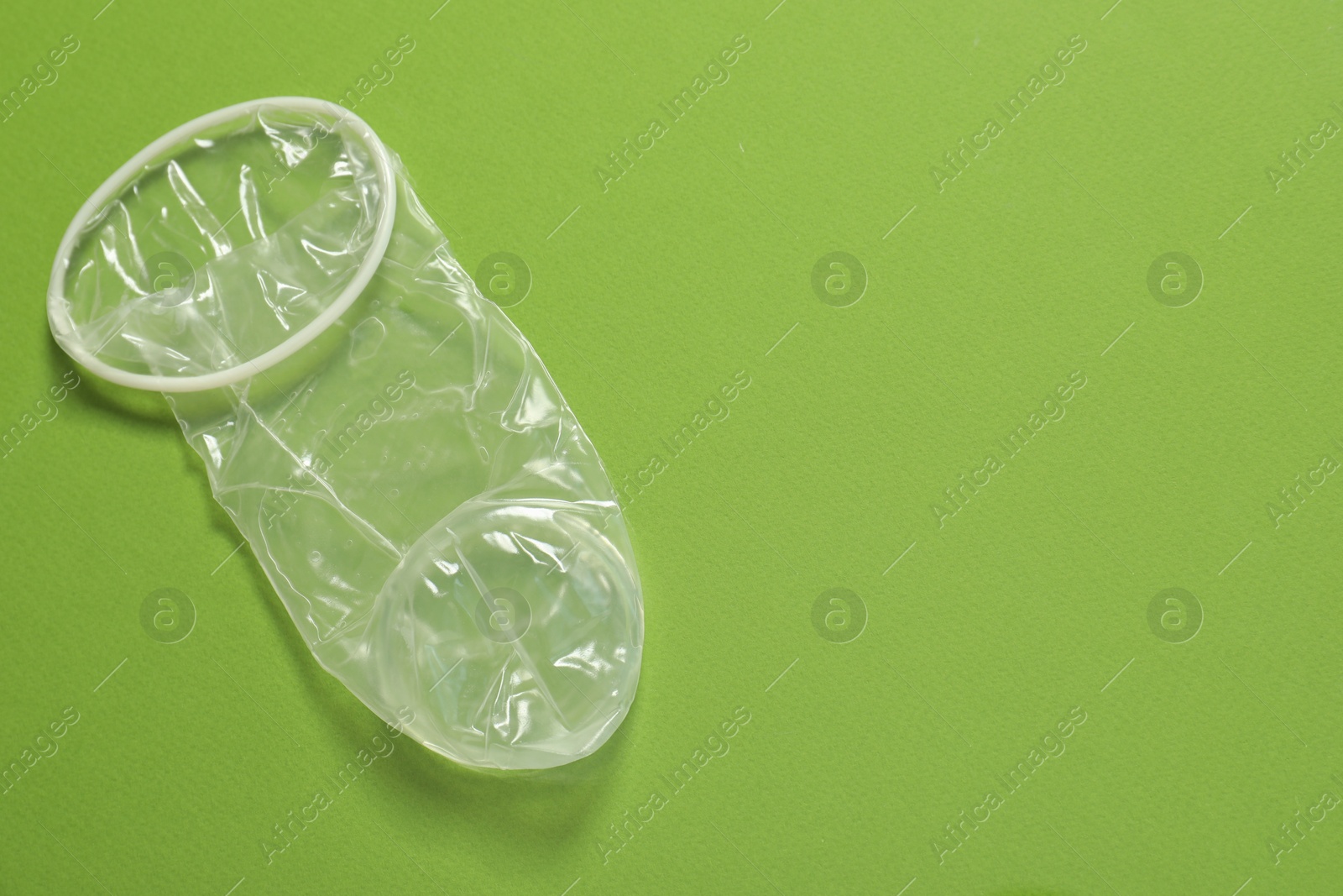 Photo of Unrolled female condom on green background, above view and space for text. Safe sex