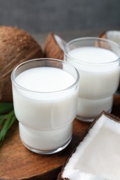 Glasses of delicious coconut milk, palm leaf and coconuts on wooden board