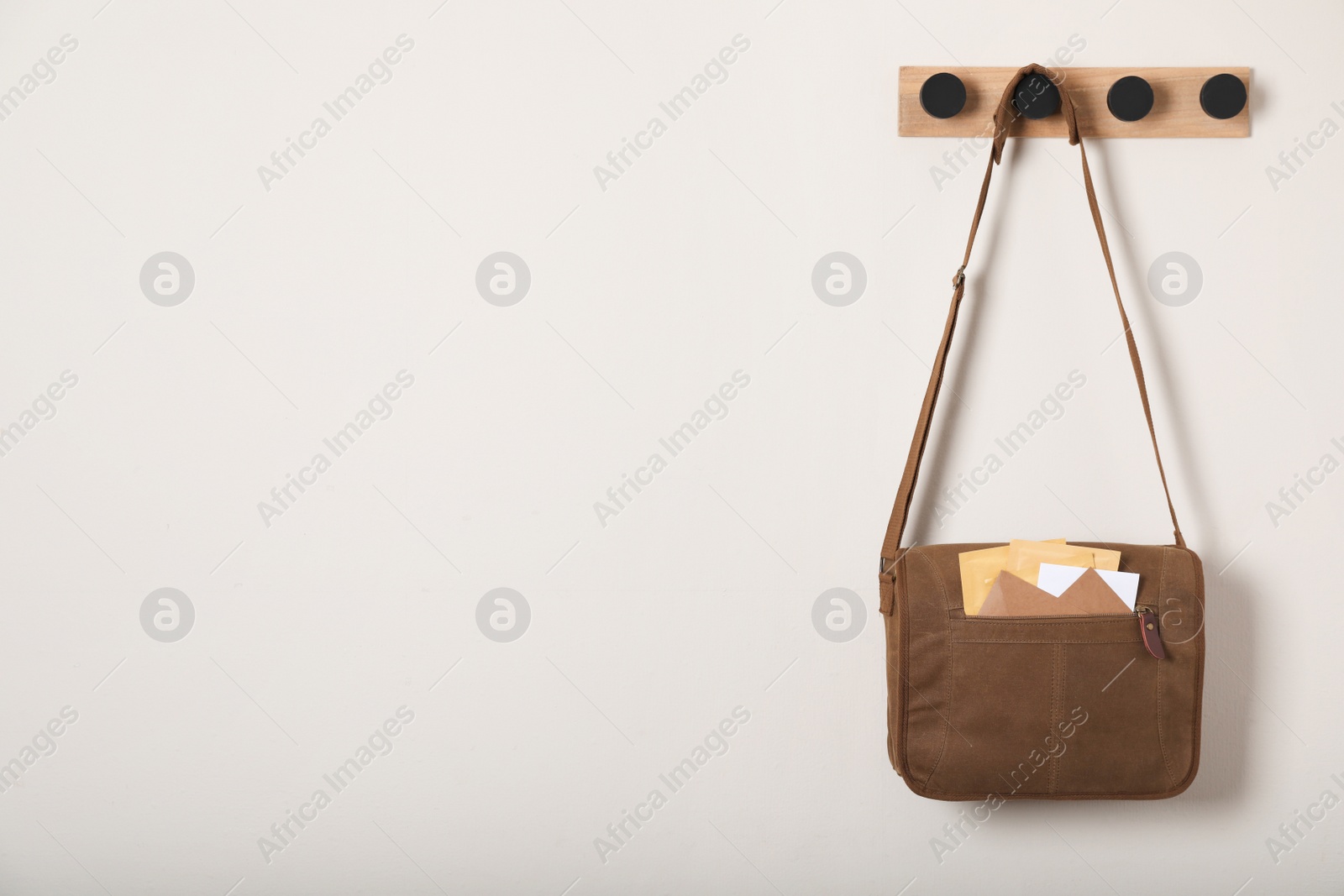 Photo of Brown postman bag with mails hanging on light wall, space for text