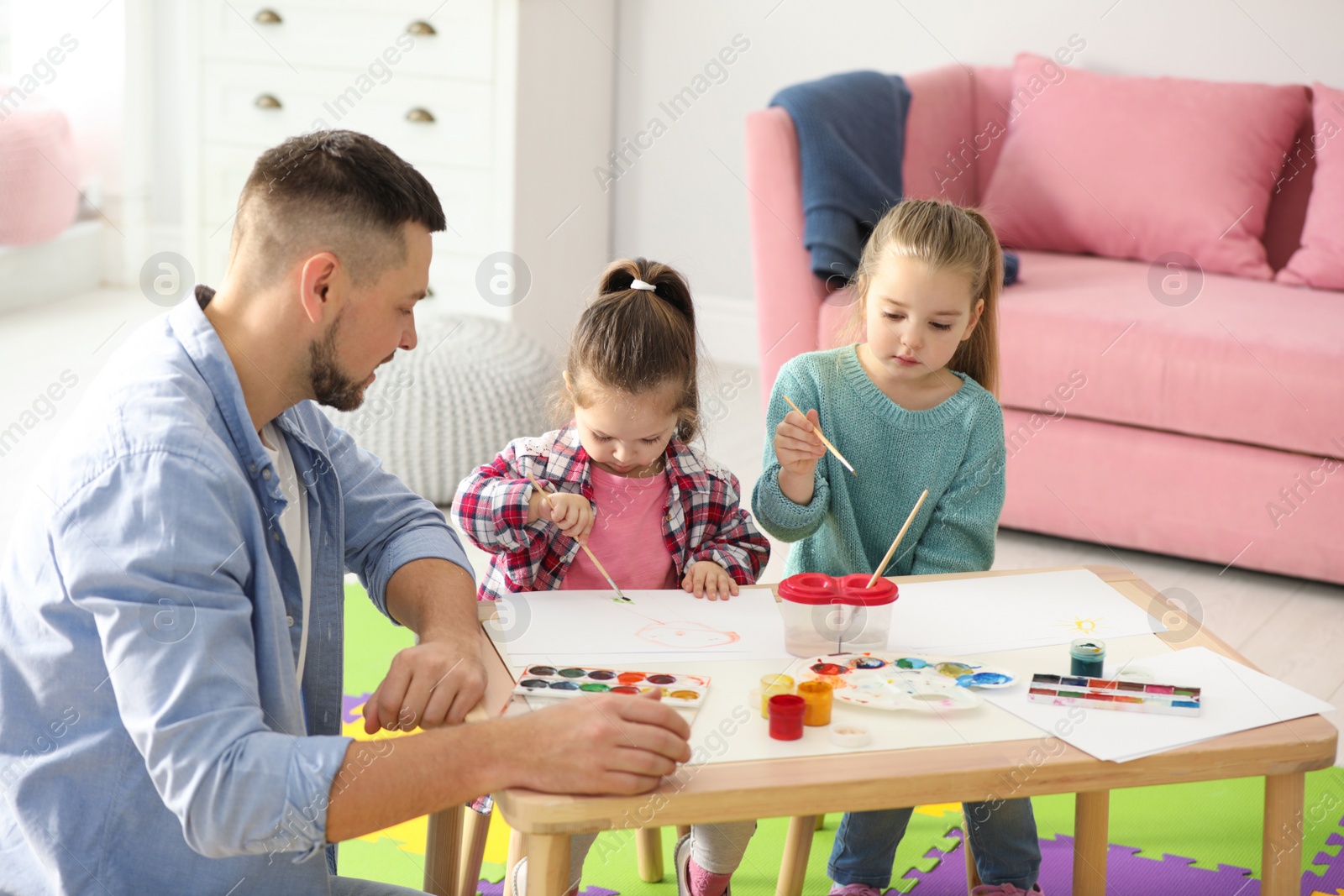 Photo of Father and daughters painting at table indoors. Playing with children