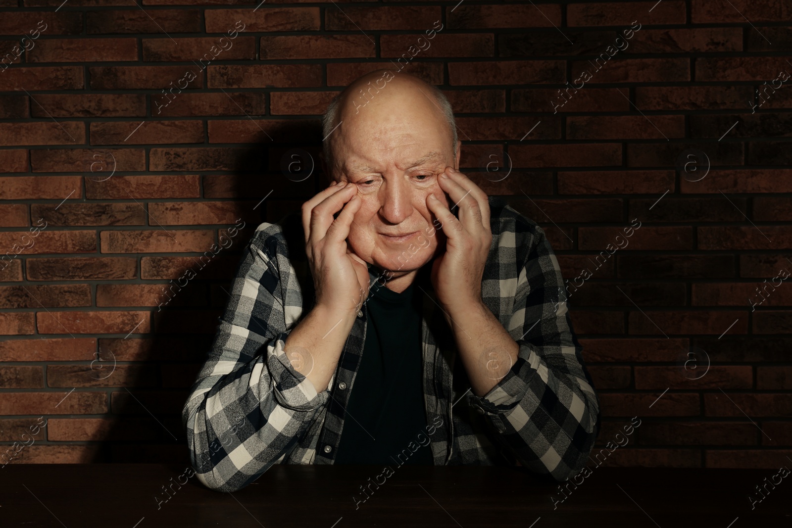 Photo of Poor senior man sitting at table near brick wall