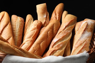 Photo of Fresh tasty baguettes in basket against black background, closeup