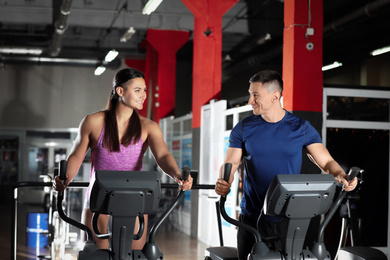 Couple working out on elliptical trainers in gym