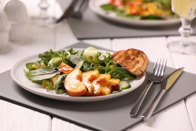 Delicious salad with peach slices served on white wooden table