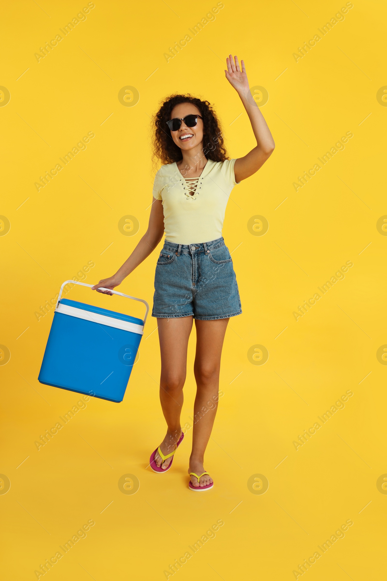 Photo of Happy young African American woman with cool box on yellow background