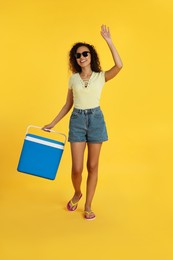 Photo of Happy young African American woman with cool box on yellow background