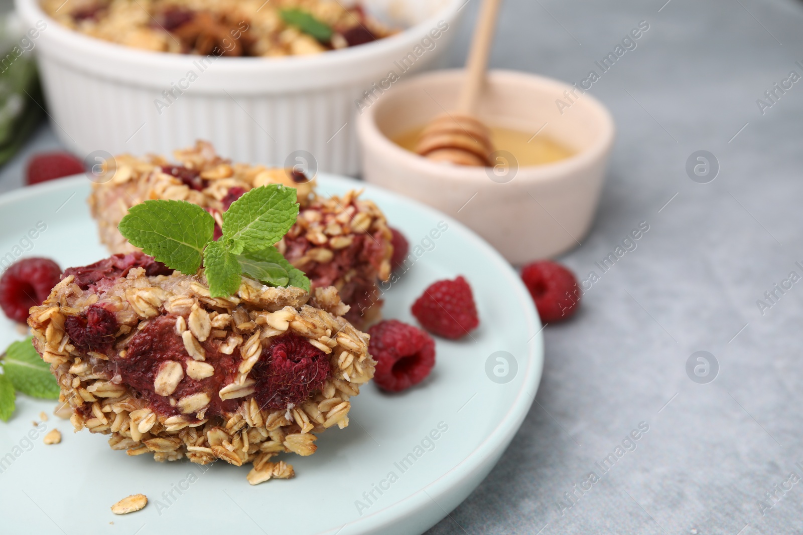 Photo of Tasty baked oatmeal with raspberries on light grey table, closeup. Space for text