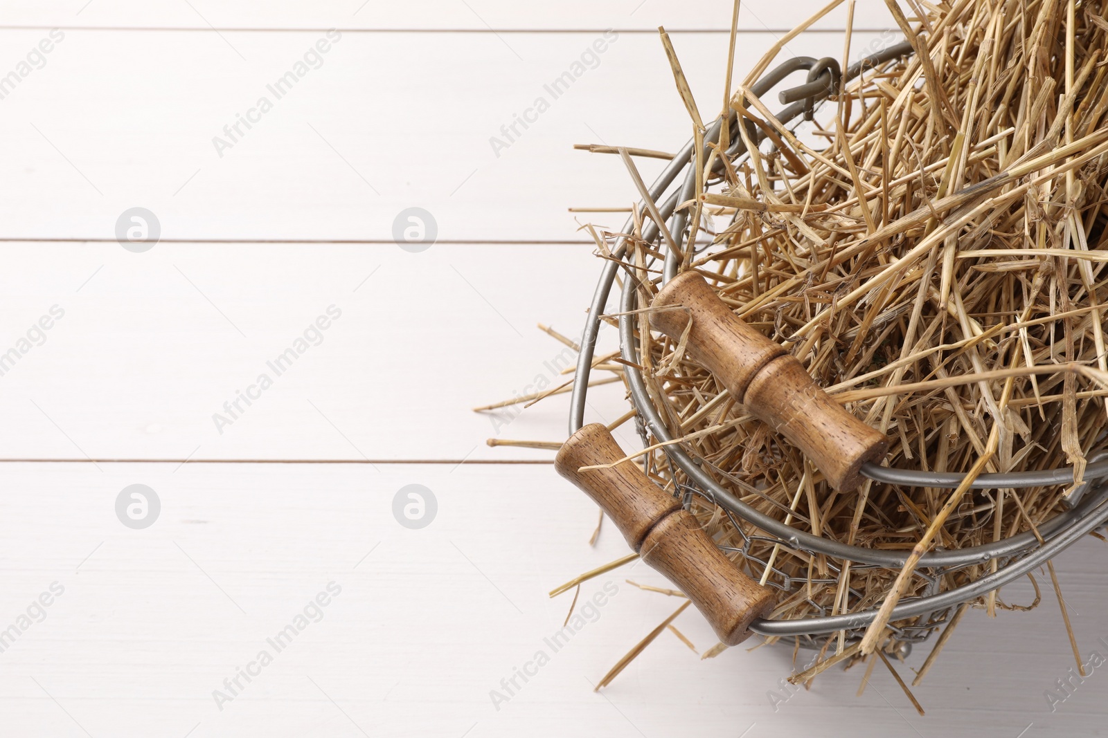 Photo of Dried straw in metal basket on white wooden table, space for text