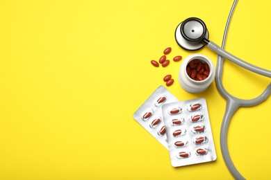 Stethoscope and pills on yellow background, flat lay with space for text