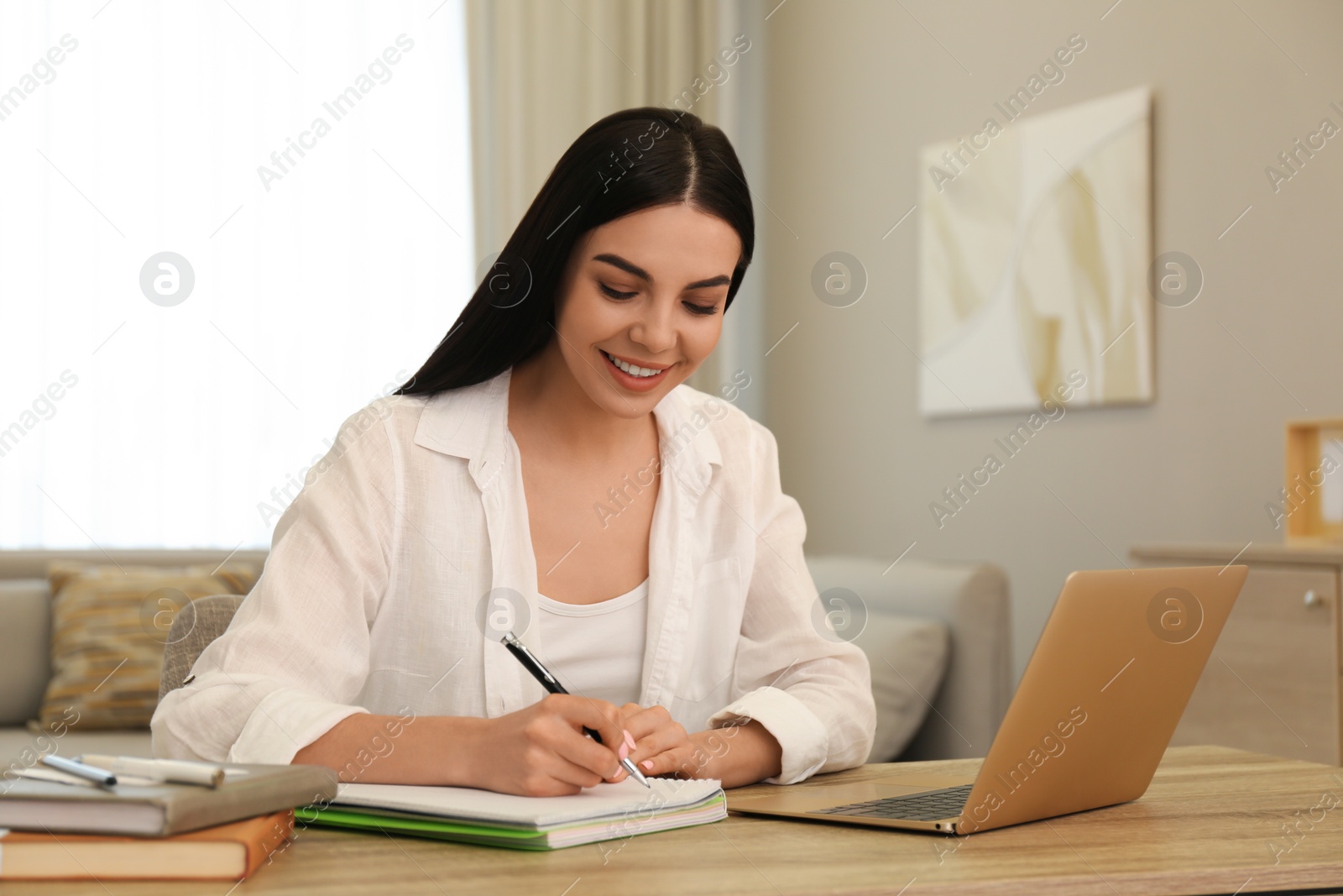 Photo of Young woman taking notes during online webinar at table indoors