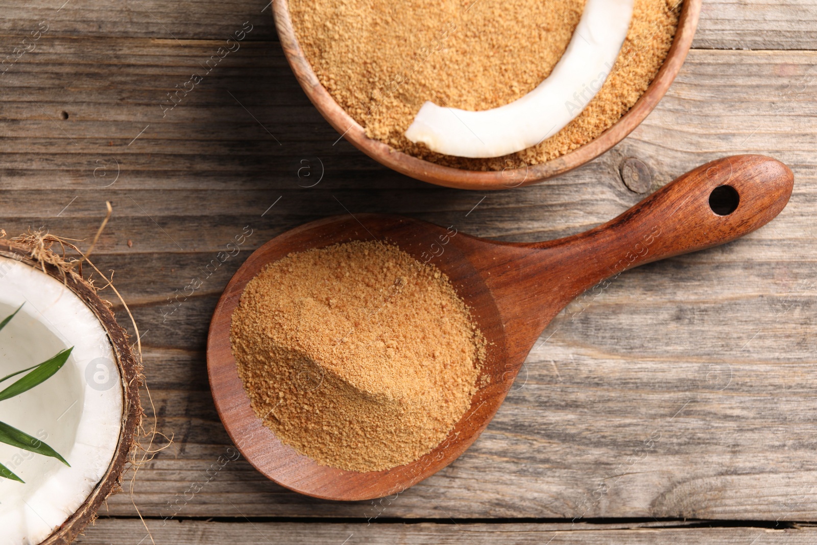 Photo of Coconut sugar in bowl, spoon and fruit on wooden table, flat lay