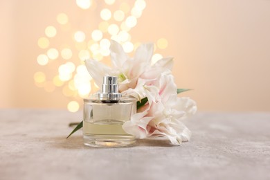 Bottle of perfume and beautiful lily flowers on table against beige background with blurred lights