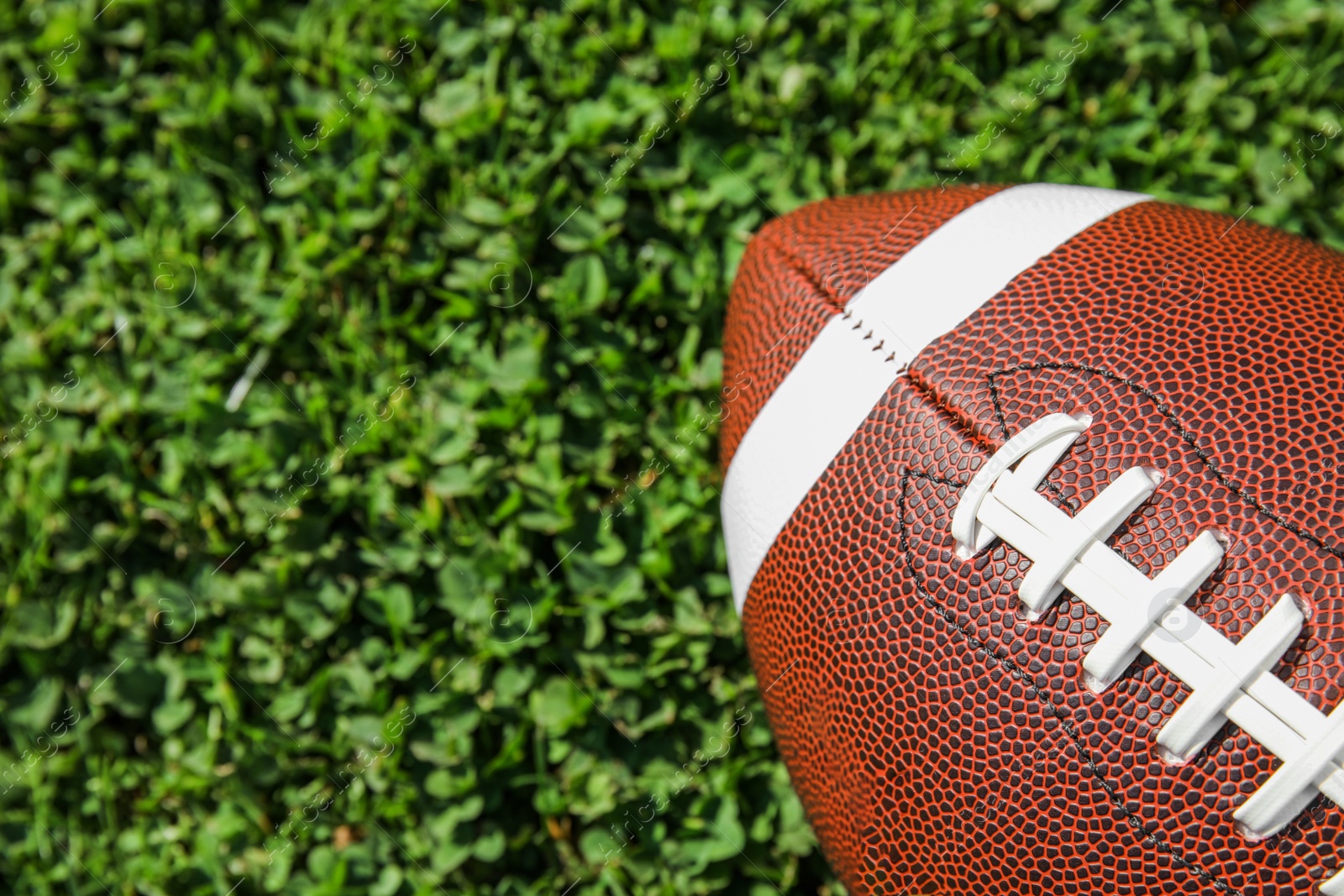 Photo of Ball for American football on fresh green field grass, top view. Space for text